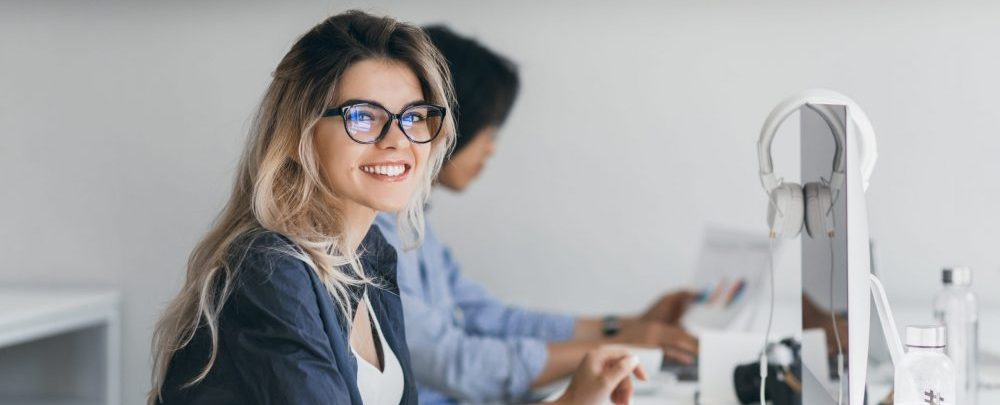 Attractive laughing freelancer girl posing with cup of coffee at her workplace